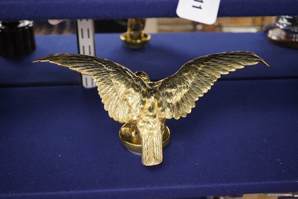 Two brass car mascots in the form of eagles, one mounted on a threaded radiator cap, the other mounted on a wooden base, the larger with a wingspan of 31cm. Condition - fair, one eagle with bent wing.